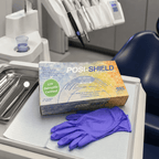 A box of PosiShield Professional nitrile gloves sits on a dental tray next to a single purple glove, with dental tools and a chair visible in the background.